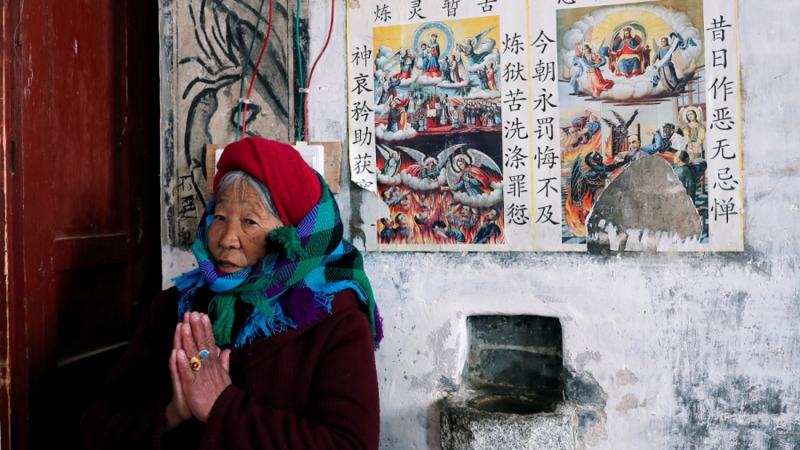 Catholic Tibetan Woman prays. An elderly Tibetan woman prays inside a church in front of religious photos with captions in Mandarin.