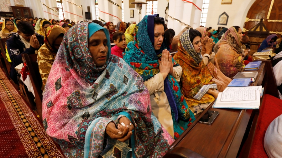 Women pray on Christmas in Pakistan. Women in colorful traditional dresses sit down and pray inside a church.