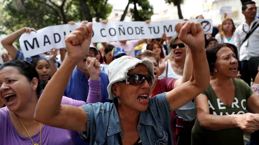 A woman holders her fists in the air. She is surrounded by other protestors.