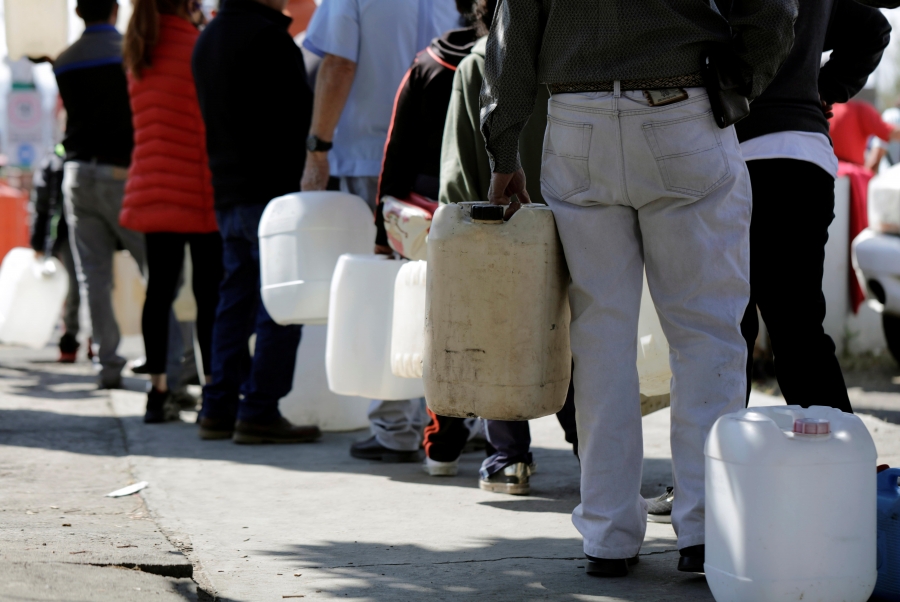 People hold empty containers while standing in line at a gas station