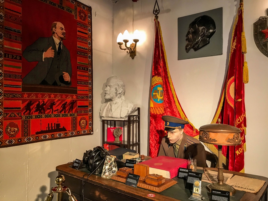 The museum’s recreation of a KGB office doubles as a Soviet time capsule, down to the iconic “perpetual” desktop calendar (a staple for Soviet citizens) and a copy of the Communist newspaper, Pravda. The museum’s recreation of a KGB office featuring a desktop calendar and a copy of the Communist newspaper, Pravda, with flags shown behind a uniformed mannequin.