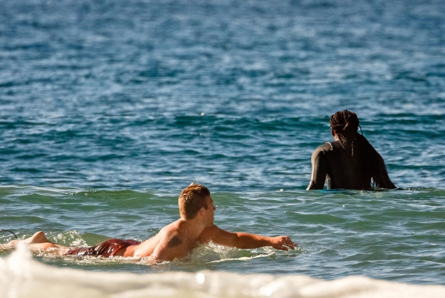 A woman waits for a wave and another surfer paddles behind her.