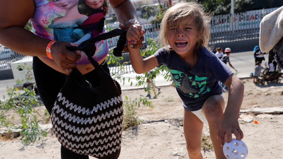 A mother and daughter run away from tear gas released by US Border Patrol near the border wall between the US and Mexico, in Tijuana, Mexico, Nov. 25, 2018. A small girl in a t-shirt with bare legs and feet cries she and her mother run up a dirt hill.