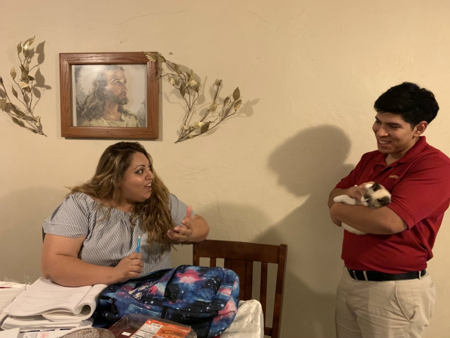 A woman is sitting on a kitchen table chair looking up and talking to her son, who is standing by the table.