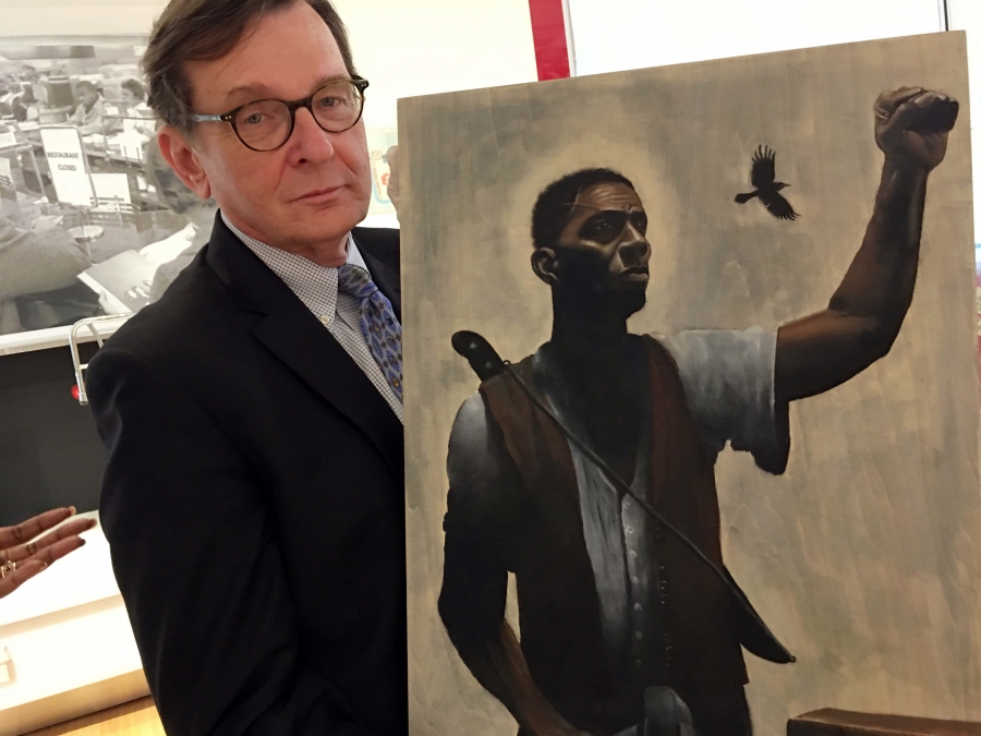 Gabriel painting A white man in glasses and a suit holds a painting of a black man with a raised fist wearing a shirt and vest.