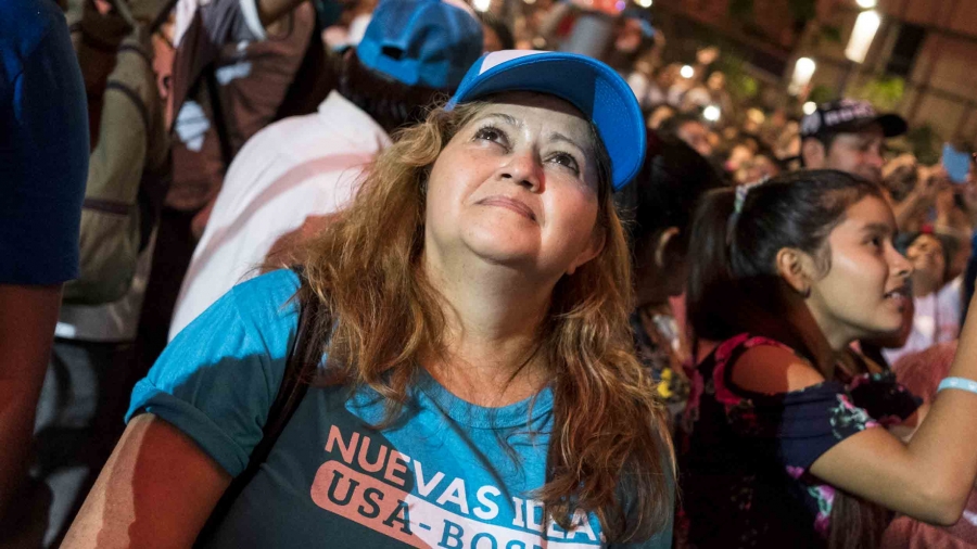A woman wearing blue looks up at a rally in San Salvador.