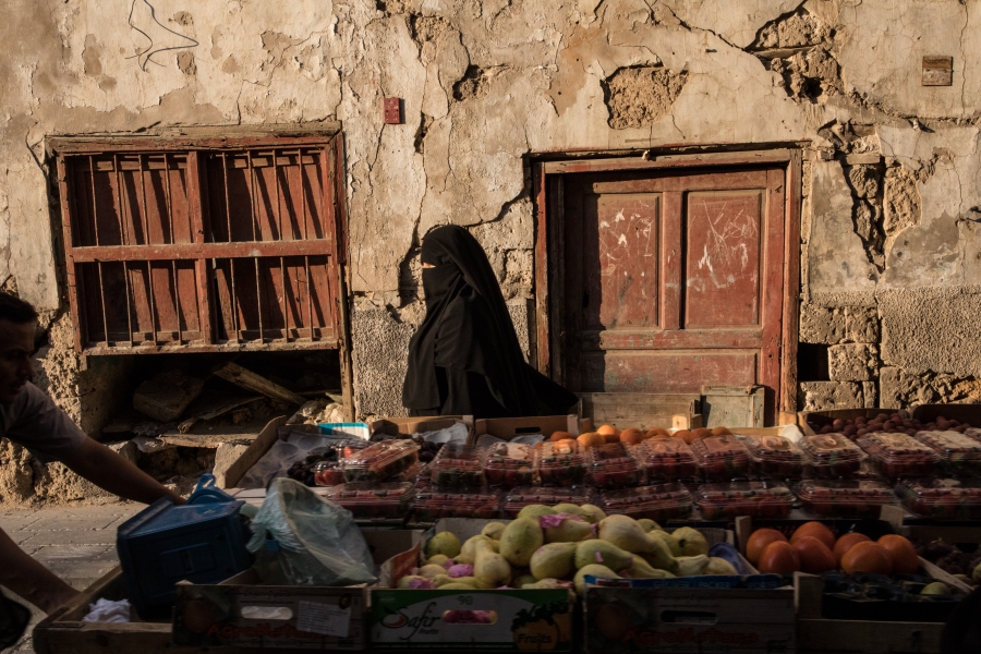A woman passes a cart carrying produce in Al-Balad, Jeddah. A woman passes a cart carrying produce in Al-Balad, Jeddah.