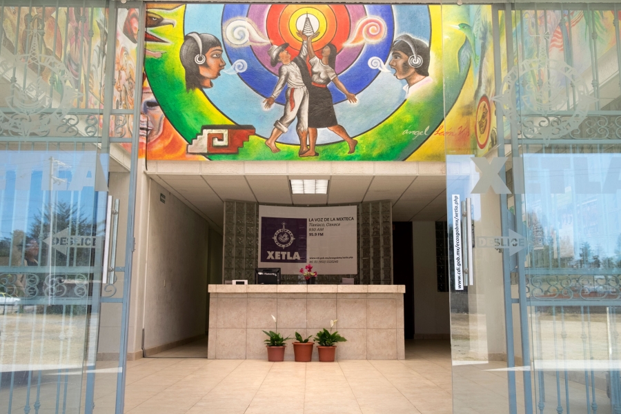 The lobby at XETLA, the radio station that airs “La Hora Mixteca.” The lobby at XETLA is shown with a desk center frame under a colorful mural.