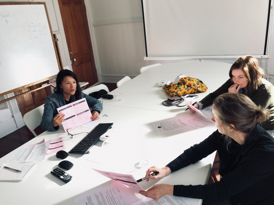 Therapists sit around a white table holding pink papers Therapists sit around a white table holding pink papers