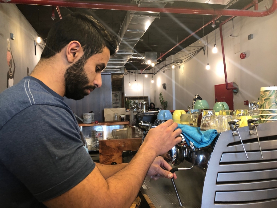 An employee at the Nabt Fenjan coffee shop in Riyadh, Saudi Arabia. A beared man wearing a blue t-shirt works the espresso machine.