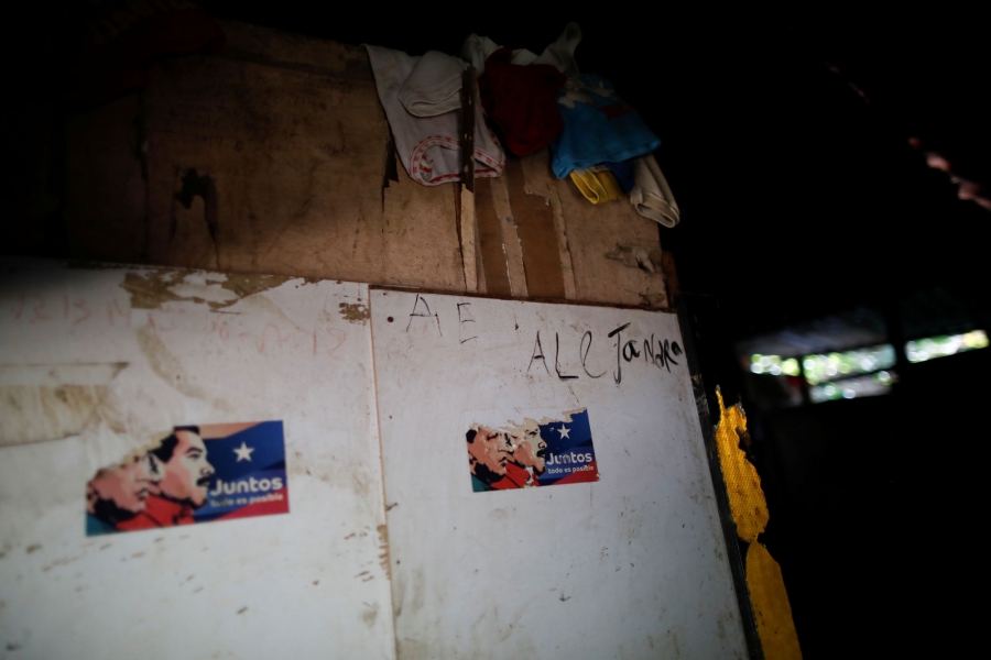 Stickers showing former President Hugo Chavez and President Nicolás Maduro are stuck to wall in Maria Guitia's home. Two partially pulled off stickers are shown with the illustrated faces of Hugo Chavez and Nicolás Maduro.