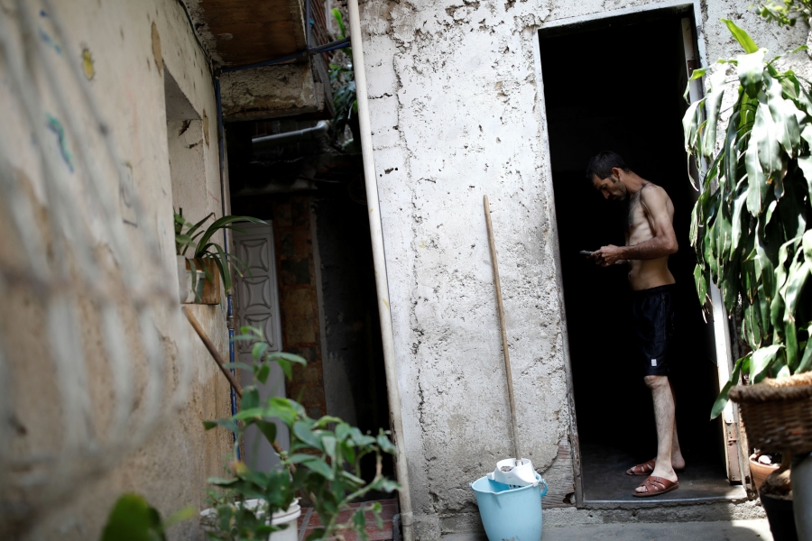 Jorge Perez looks at a phone in his mother's home. Jorge Perez is shown standing in a doorway without a shirt on, looking at a phone.