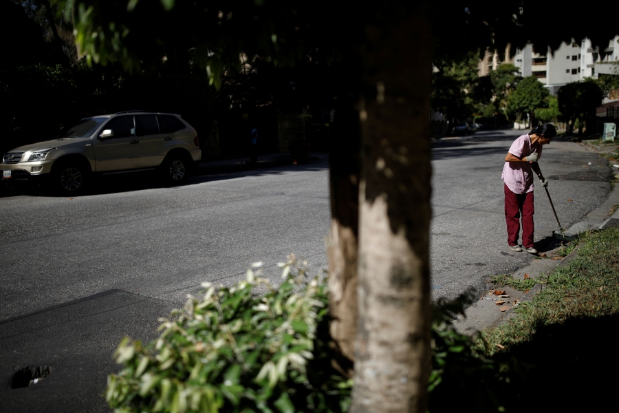 Guzman sweeps the street. A woman is shown in red pants sweeping the street.