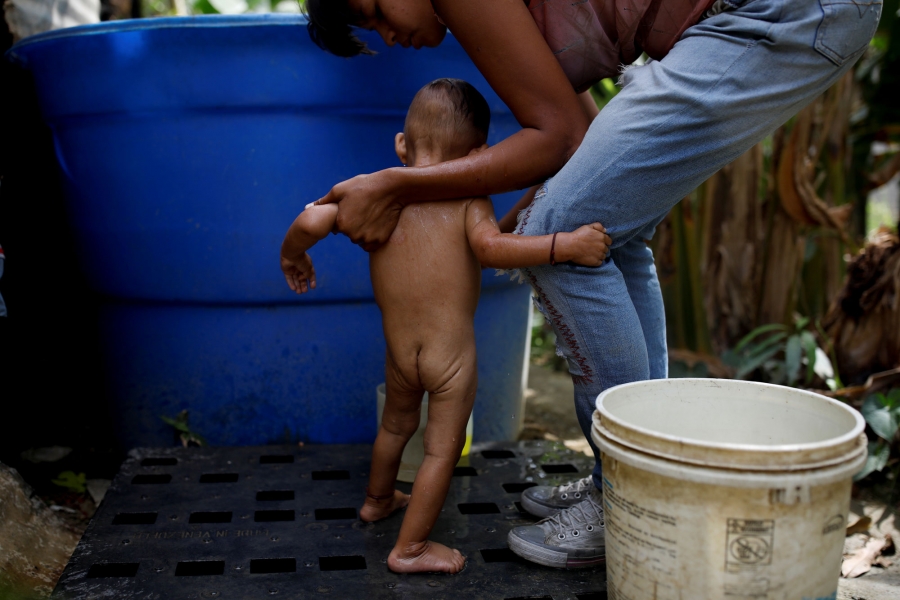 Guitia washes her son at home. A woman is shown holding the hands of her naked baby during a bath.