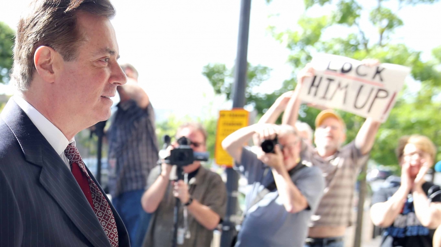 Paul Manfort wears a suit and walks past a line of protestors and photographers on his way into court