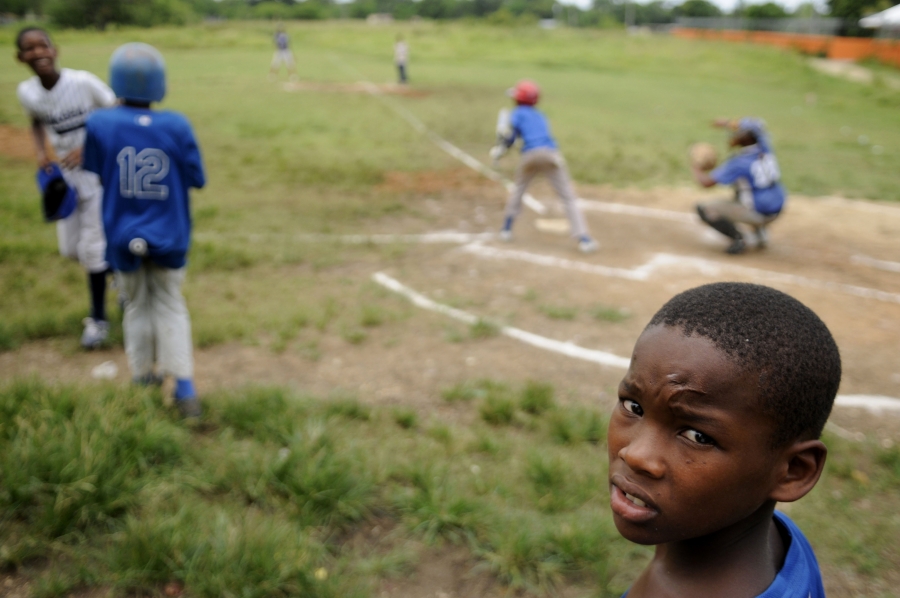 A young boy looks into a camera while others play baseball behind him
