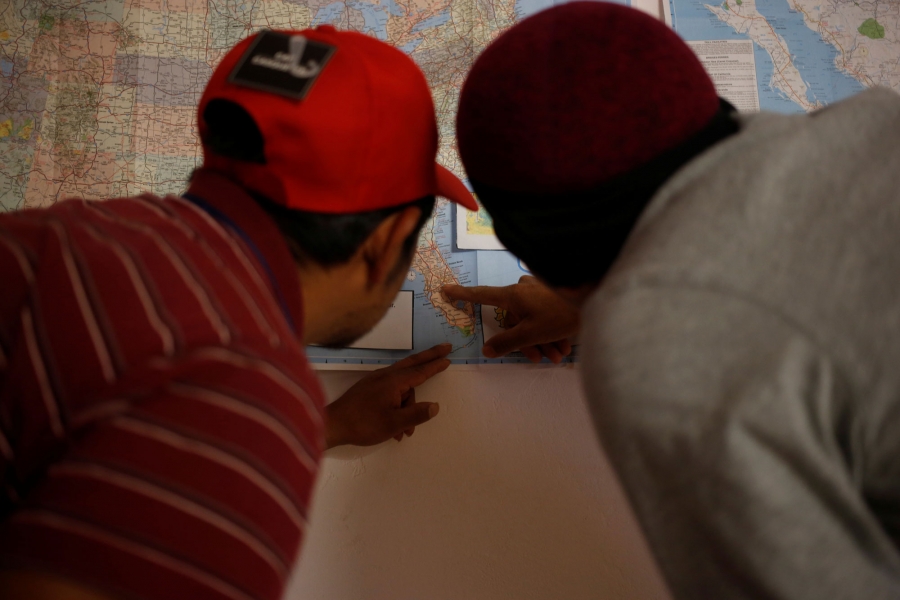 Two migrants study a US map in the monastery. Two boys are shown pointing at a map of the US highlighting Florida.