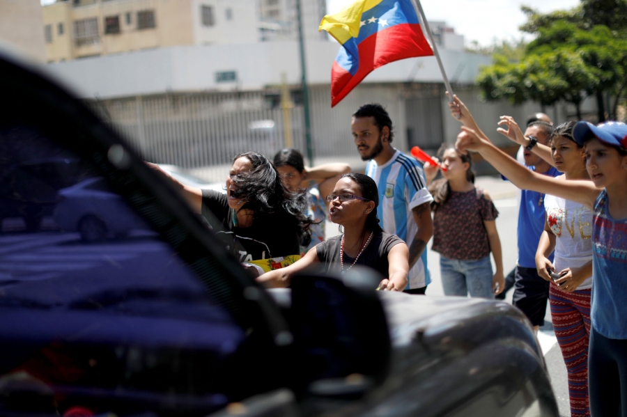 A woman reacts as she and others block a street to show their anger because of the ongoing blackout in Caracas, Venezuela. A group of people are shown trying to block a car from driving down a road.