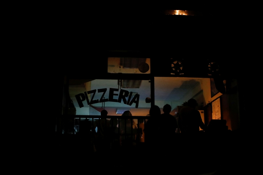 People eat by candlelight at a pizzeria during the blackout in Caracas, Venezuela. A darkened pizza shop is shown with patrons eating by candlelight.