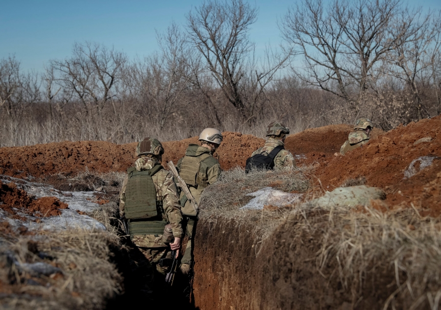 Members of Ukraine's interior ministry's Azov battalion walk at a frontline near the village of Travneve. Four men in military fatigues and helmets are shown in a trench walking.