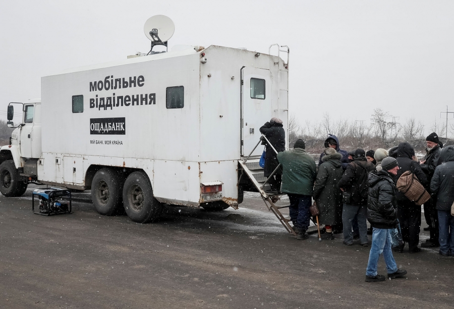 Local residents stand in line to an ATM located in an armored truck after crossing the contact line between pro-Russian rebels and Ukrainian troops near the frontline in Mayorsk. A large white armored truck is shown with a long line of people behind it.