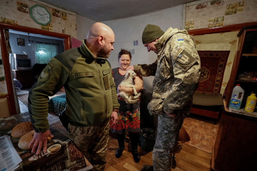 Ukrainian servicemen play with a small goat as they deliver bread to a local resident in the village of Zaitseve. Two Ukrainian servicemen are shown on either side of a woman holding a small goat.
