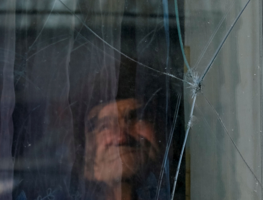 Yushkov looks at an impact of bullet in a window of his house. A person is shown blurry behind a pane of glass that has a hole in it.