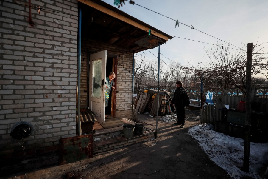 Yushkov speaks with his neighbor. A woman is shown standing in the doorway of her house with her white door ajar.