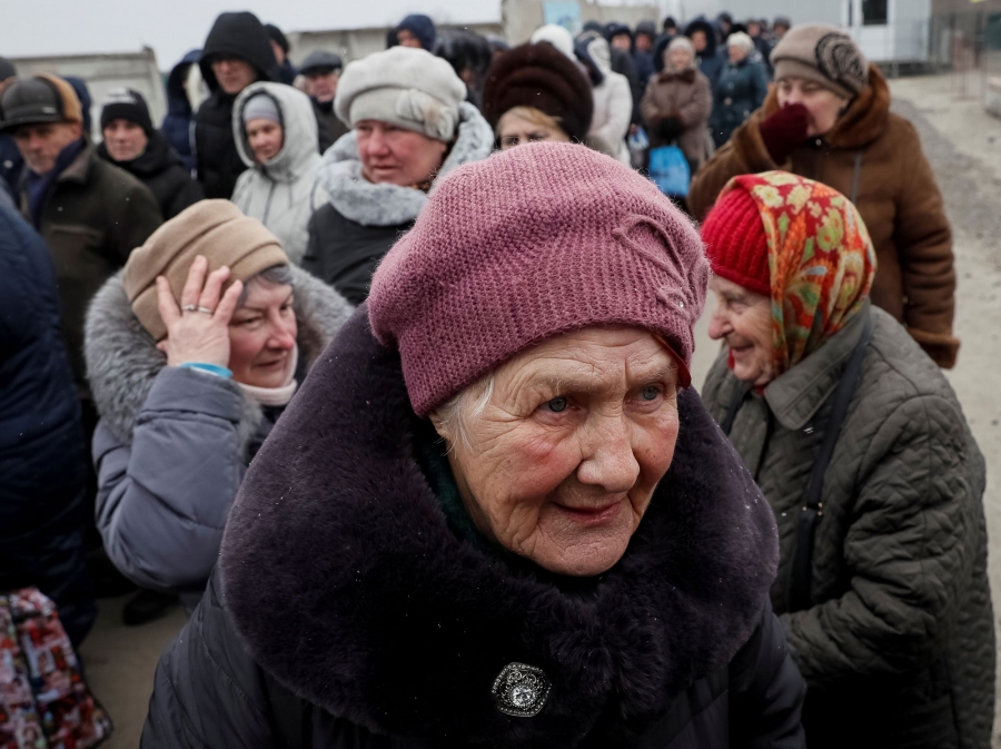 People line up as they wait at passport control after crossing the contact line between pro-Russian rebels and Ukrainian troops. A group of people are shown with an older woman in the front wearing a pink winter hat and fur jacket.
