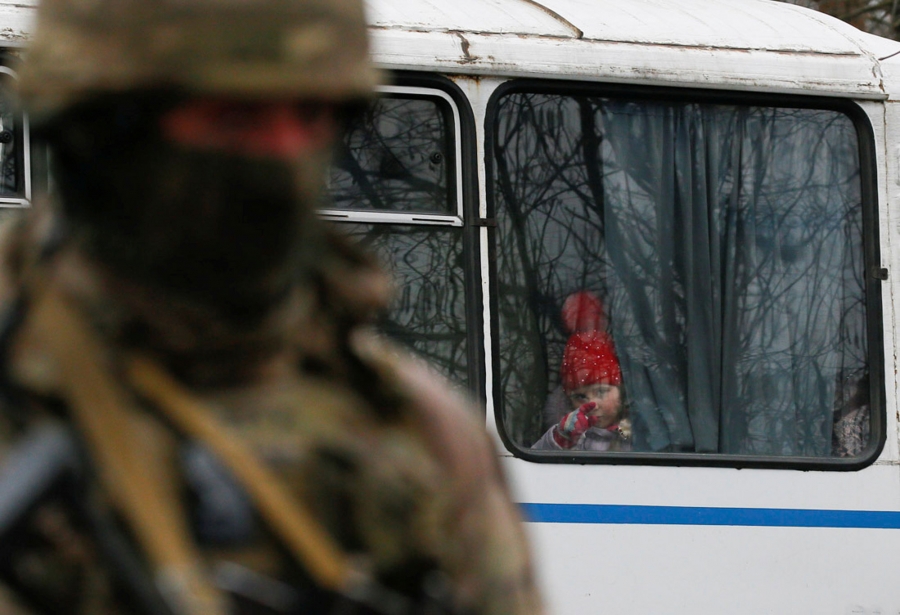 A girl looks out of a bus window which crosses the contact line between pro-Russian rebels and Ukrainian troops as Ukrainian border guard stands by in Mayorsk. A girl is a red hat looks out of a bus window pointing her finger.