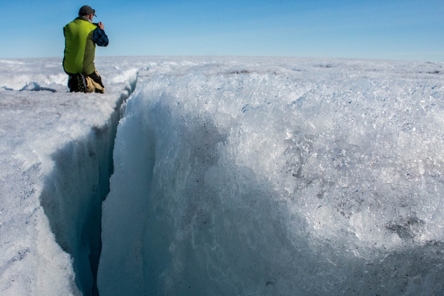 University of Montana glaciologist Joel Harper examines a deep crack in the ice sheet called a crevasse. University of Montana glaciologist Joel Harper is shown knealing next to a deep crack in the ice sheet called a crevasse.