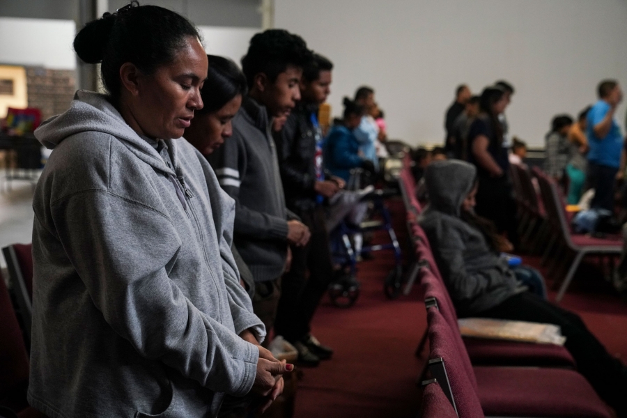Central American asylum seekers attend a religious service at the church Caminos de Vida, which is a temporary shelter in El Paso, Texas. Several people are shown with their hands folded and heads bowed in prayer.