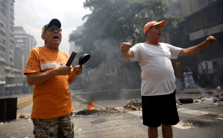 Demonstrators shout at a protest against the government of Venezuelan President Nicolás Maduro in Caracas, Venezuela March 31, 2019. A demonstrators wearing an orange shirt stand with a small pan in his hand next to another protester in a white t-shirt and orange hat.