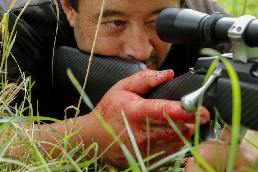 Noel Womersley lies down to shoot a cow with his rifle before butchering it outside Christchurch, New Zealand. Noel Womersley is shown in a close-up photo laying down with his bloodied-hand around his gun.