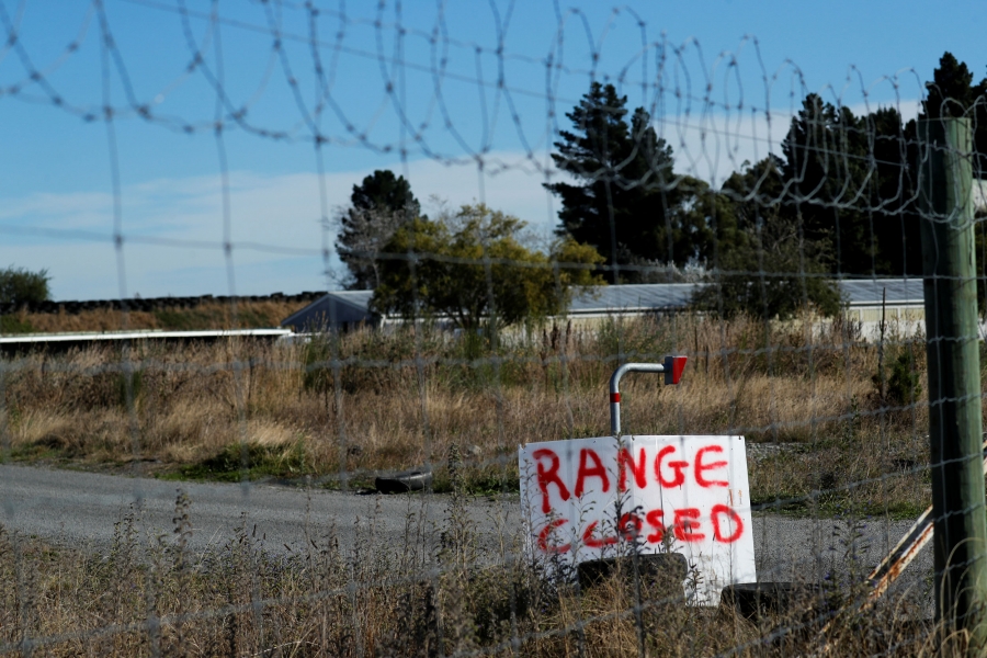 A sign is seen at a closed shooting range outside Christchurch, New Zealand. A sign is seen through a chain link fence with a wooden sign reading, "range closed."