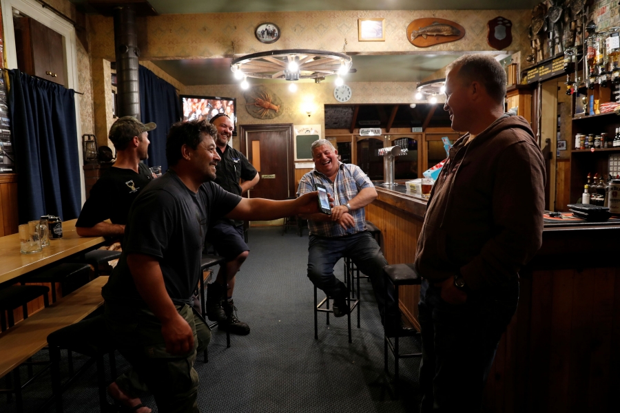 Noel Womersley smiles with friends in a pub after a hunter club meeting in Sefton, New Zealand. Noel Womersley smiles and shows a picture on his mobile phone to friends in a pub.