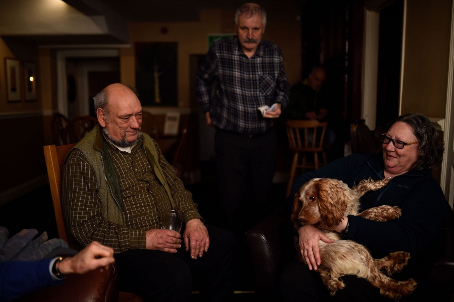 Andy Clarke, a retired Fisheries officer in the Environment Agency who voted to leave the EU, has a pint of ale with his friends. An older man is shown sitting down, wearing a vest and holding a glass next to a woman holding a dog.