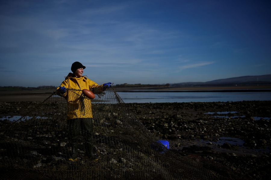 Owen takes in her nets. A woman is shown in a yellow jacket and dark hat while holding a net.