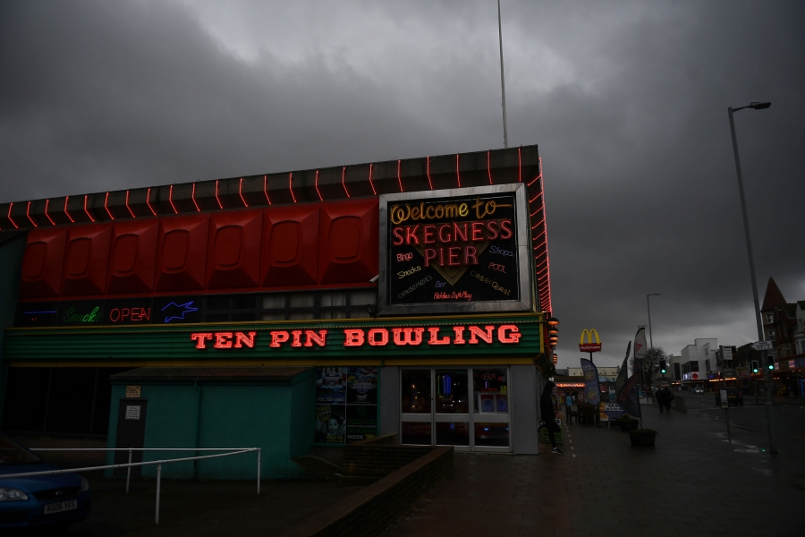 A Ten Pin Bowling sign is illuminated on the side of an amusement arcade in Skegness. The facade of a bowling alley is shown illuminated with neon lights.