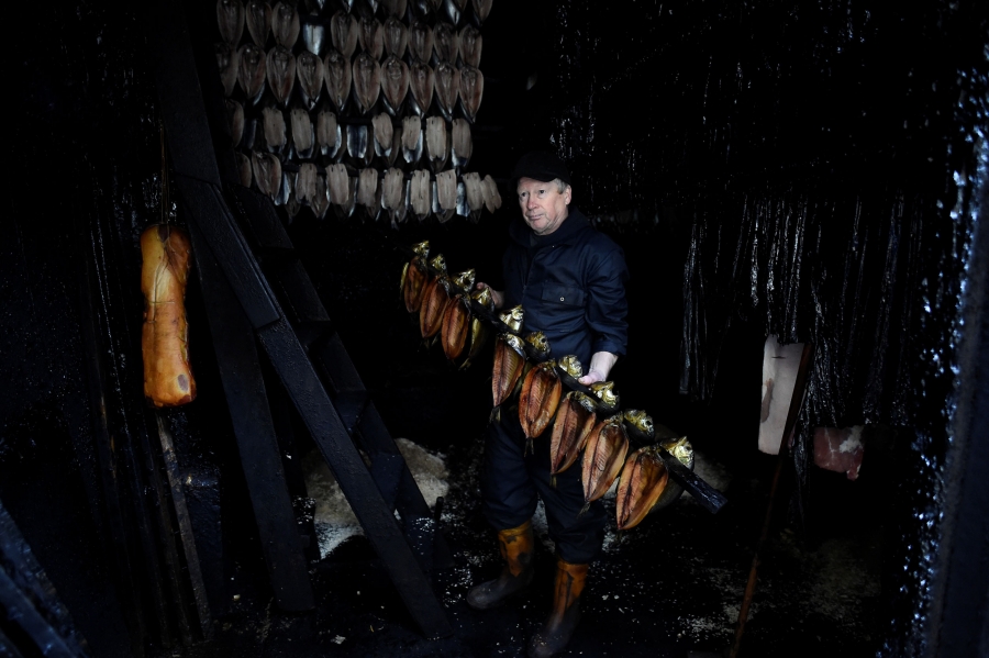 Brown holds some kippers in the smoking room. A man is shown standing in the middle of kipper herring hung on lines while being smoked.