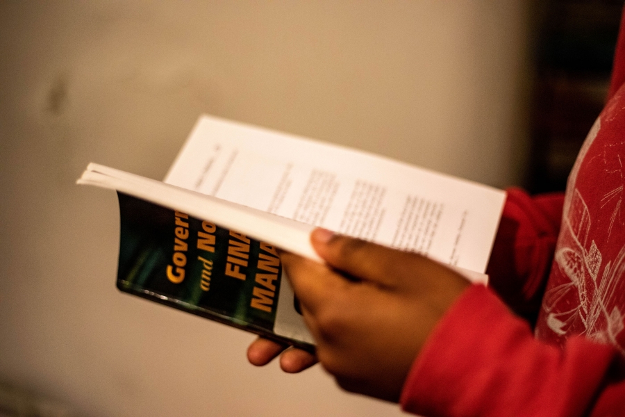 Kettly stands in the kitchen of her Boston home flipping through one of her textbooks for her master's program. A close-up photograph of a woman holding a textbook with the word "Government" printed on it.