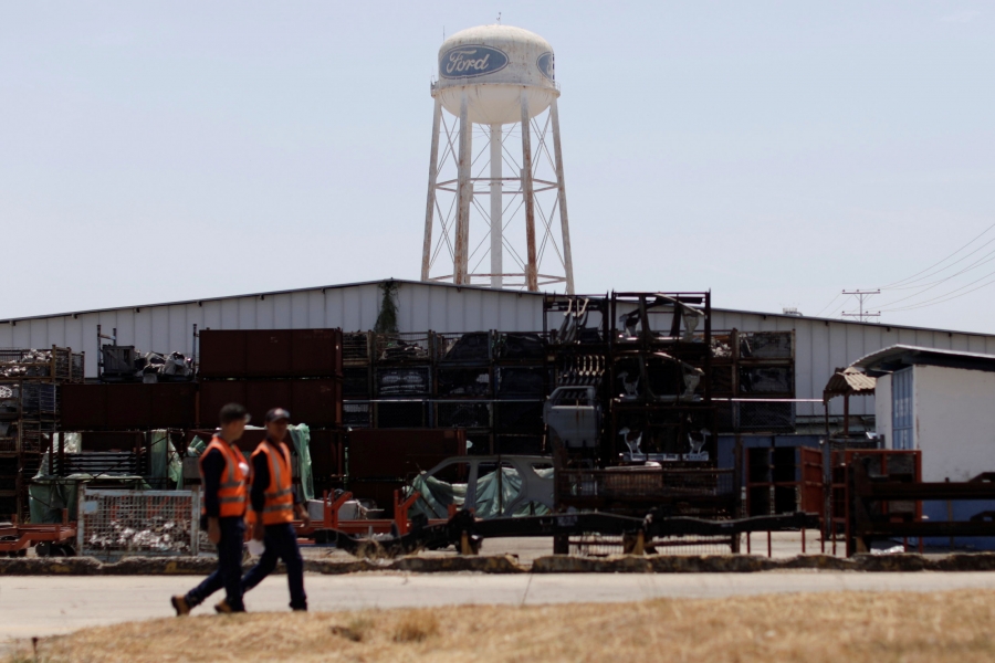 Men walk at a Ford plant in Valencia, Venezuela. Two men are shown wearing reflective safety vests while walking at a Ford plant.