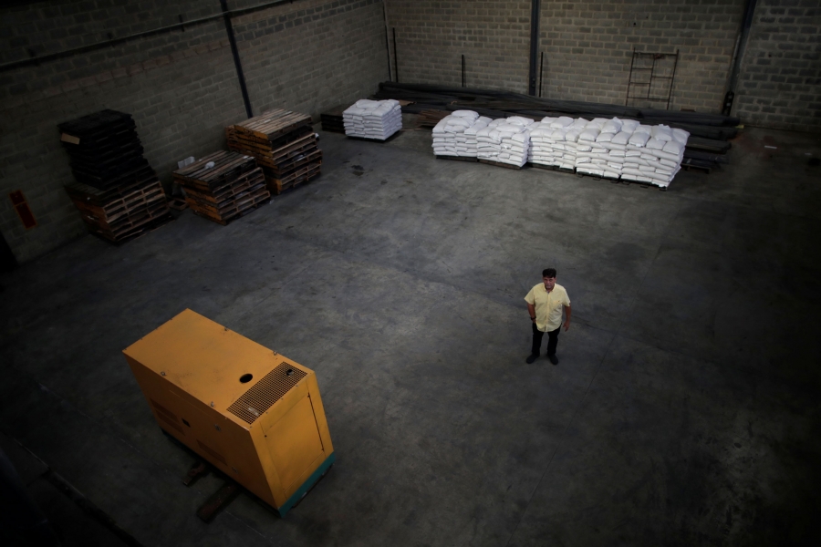 Businessman Antonello Lorusso stands next to a generator at the warehouse of his food packaging plant in Valencia, Venezuela. In a photograph taken from above, a man in a yellow shirt is shown standing in a nearly empty warehouse.
