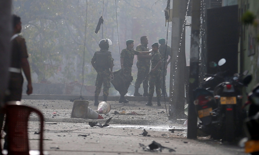 Special Task Force Bomb Squad officers inspect the site of an exploded van near a church that was attacked in Colombo, Sri Lanka. Special Task Force Bomb Squad officers are shown in the distance with debris from an explosion all over the street.