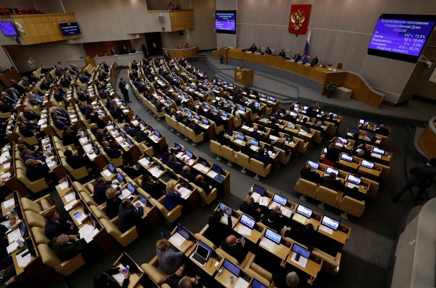 Russian lawmakers attend a session during a vote in Moscow. A large group of people are seated in chairs in a large room.