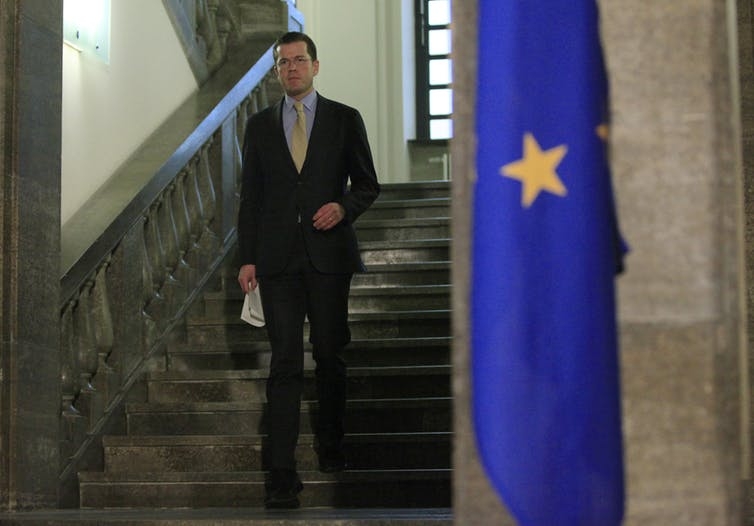 German Minister of Defense Karl-Theodor zu Guttenberg arrives at a press briefing to announce his resignation in Berlin, March 1, 2011. A man stands on a staircase next to a European Union flag.