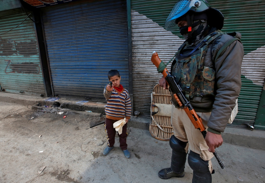 boy stands with pistol next to Indian soldier