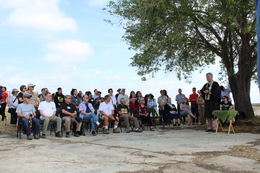 A group sits on the side as a man leads a ceremony.