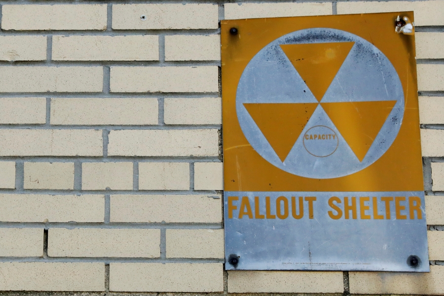 A yellow nuclear fallout shelter sign is seen hung on a brick building