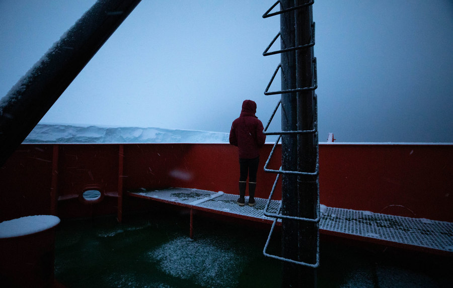Oceanographer Peter Sheehan looks out at Thwaites from the bow of the ship before sunrise on the day of arrival. Oceanographer Peter Sheehan is shown with his jacket hood over his head while looking out at Thwaites.